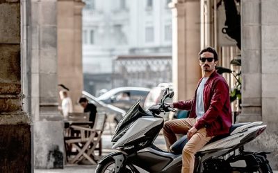 Hombre con gafas de sol sobre una moto Malaguti en una calle urbana con edificios clásicos